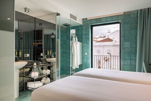 A modern hotel room with a large bed, a glass-enclosed bathroom, and a balcony with a view of buildings. - WC by The Beautique Hotels (Lisbon)