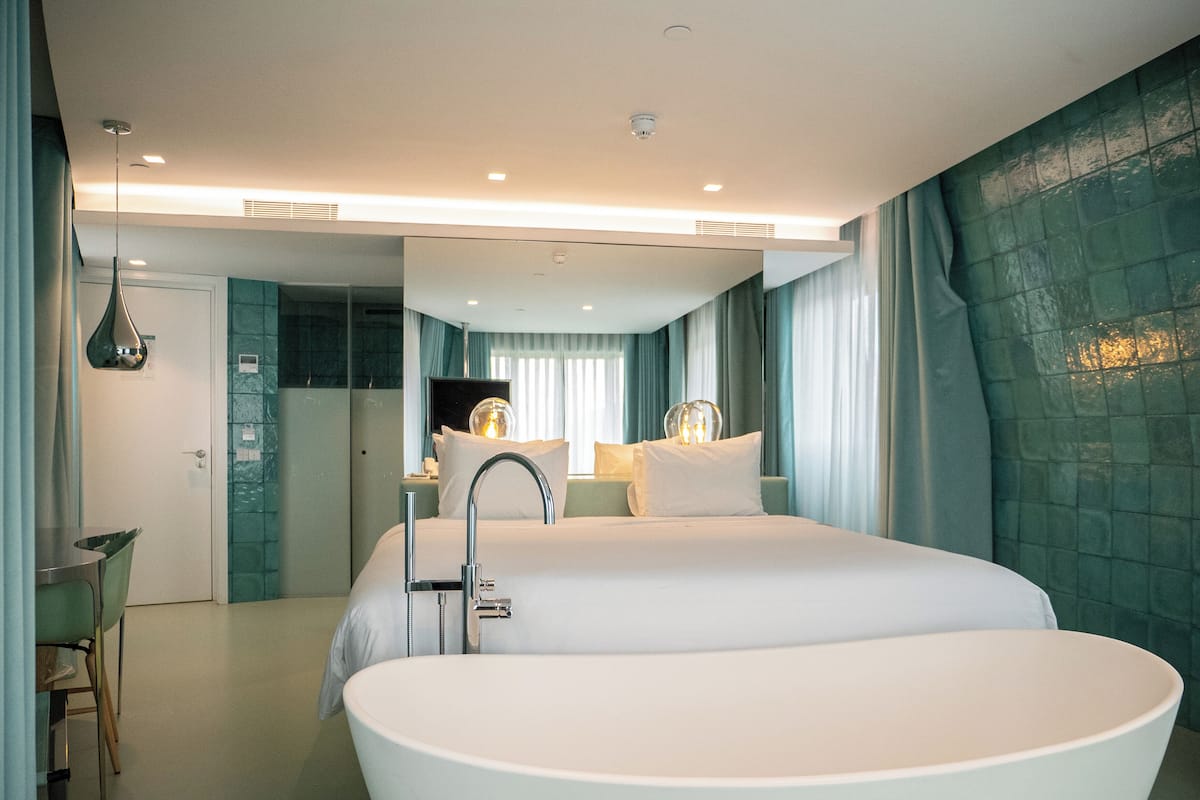 Una habitación de hotel moderna con una bañera grande, zona de ducha separada y un espacio de descanso con una silla.