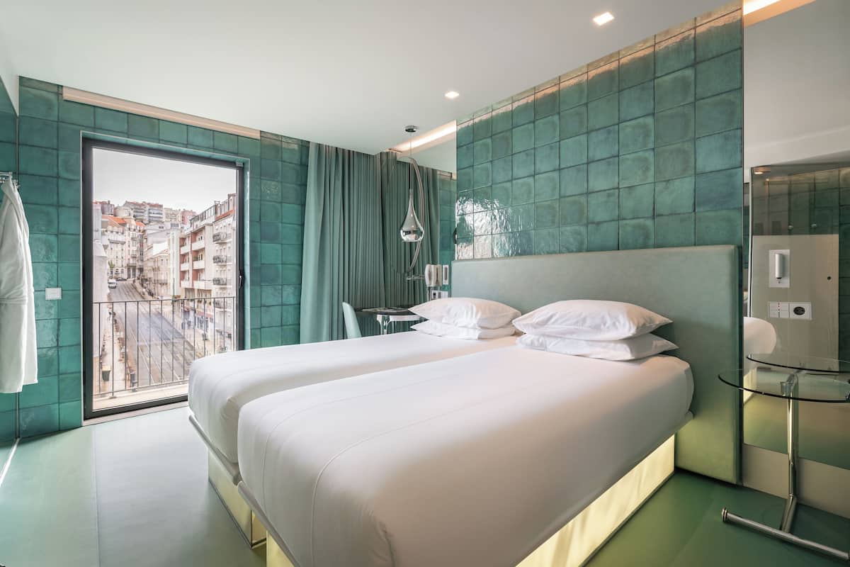 Una habitación de hotel moderna con una cama grande, una mesa de vidrio y vistas a un paisaje urbano a través de una puerta corrediza.