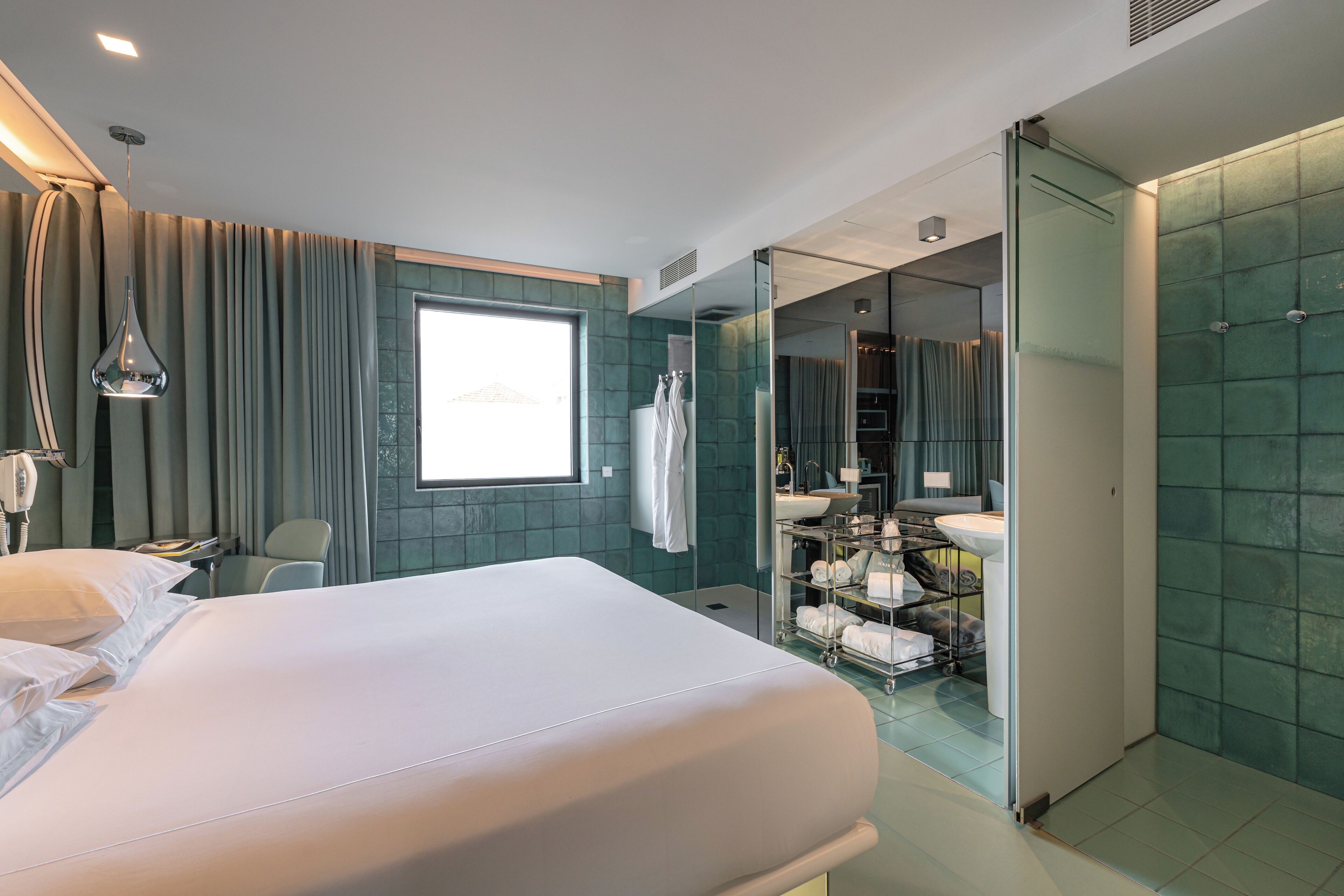 Een moderne hotelkamer met een groot bed, een badkamer met een douchewand en uitzicht op de stad.