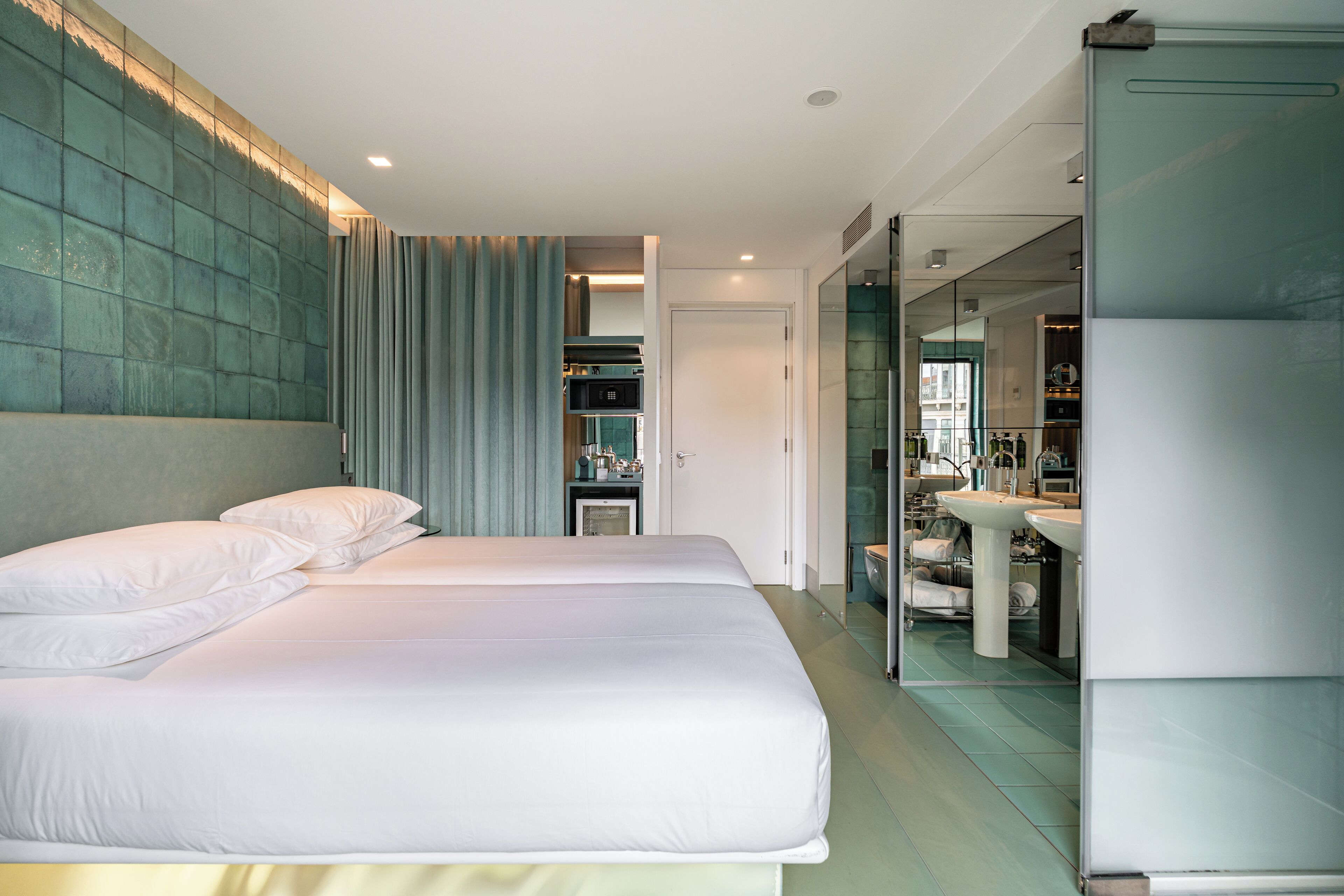 Habitación de hotel moderna con una cama grande, baño con mampara de vidrio y vista a la ciudad.