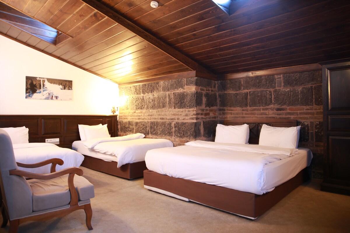 A room with three beds, a wooden ceiling, stone walls, and a chair.