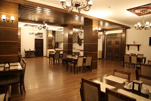 A spacious dining area with wooden flooring and multiple tables and chairs. - Cheltikov Hotel (Kars)
