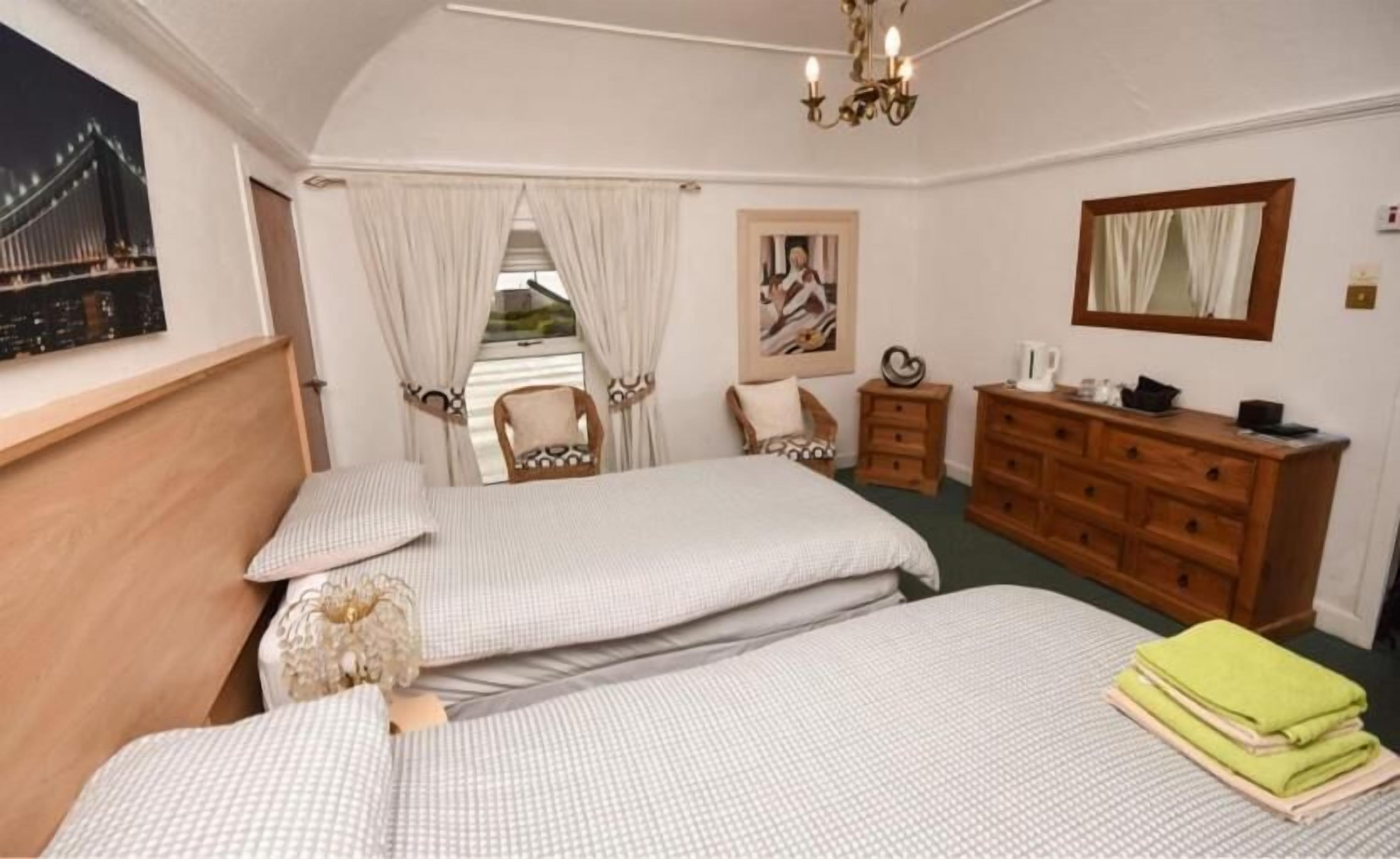 A bedroom with two beds, a dresser, a chair, and a painting.