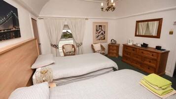 A bedroom with two beds, a dresser, a chair, and a painting.