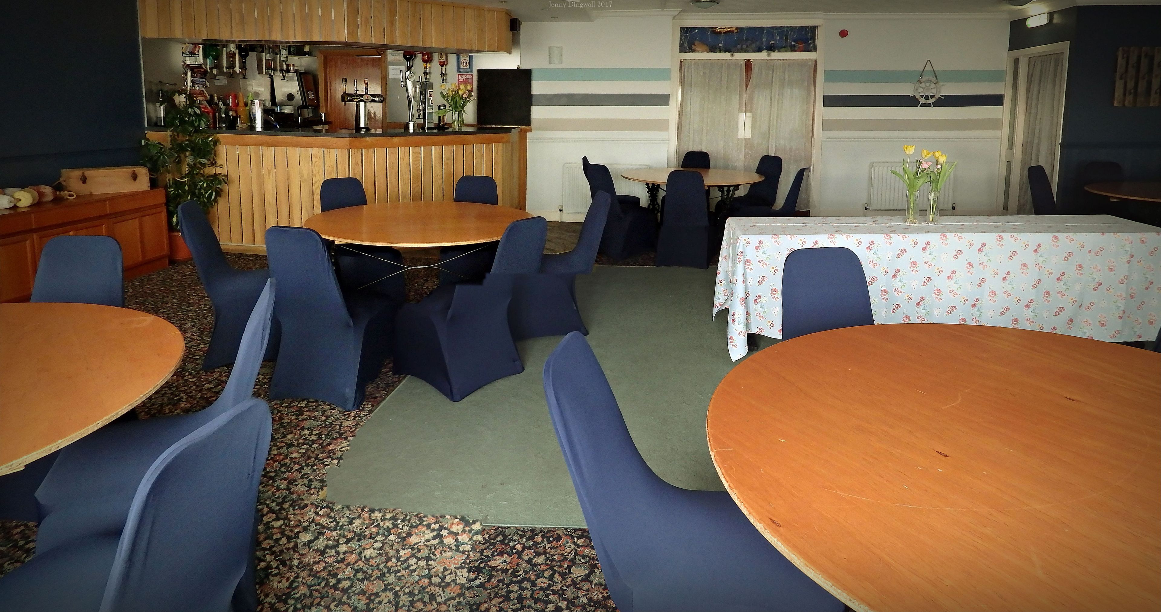 Un espace repas avec des tables rondes et des chaises bleues, un bar proposant une variété de boissons et de plats, et un mur à rayures.
