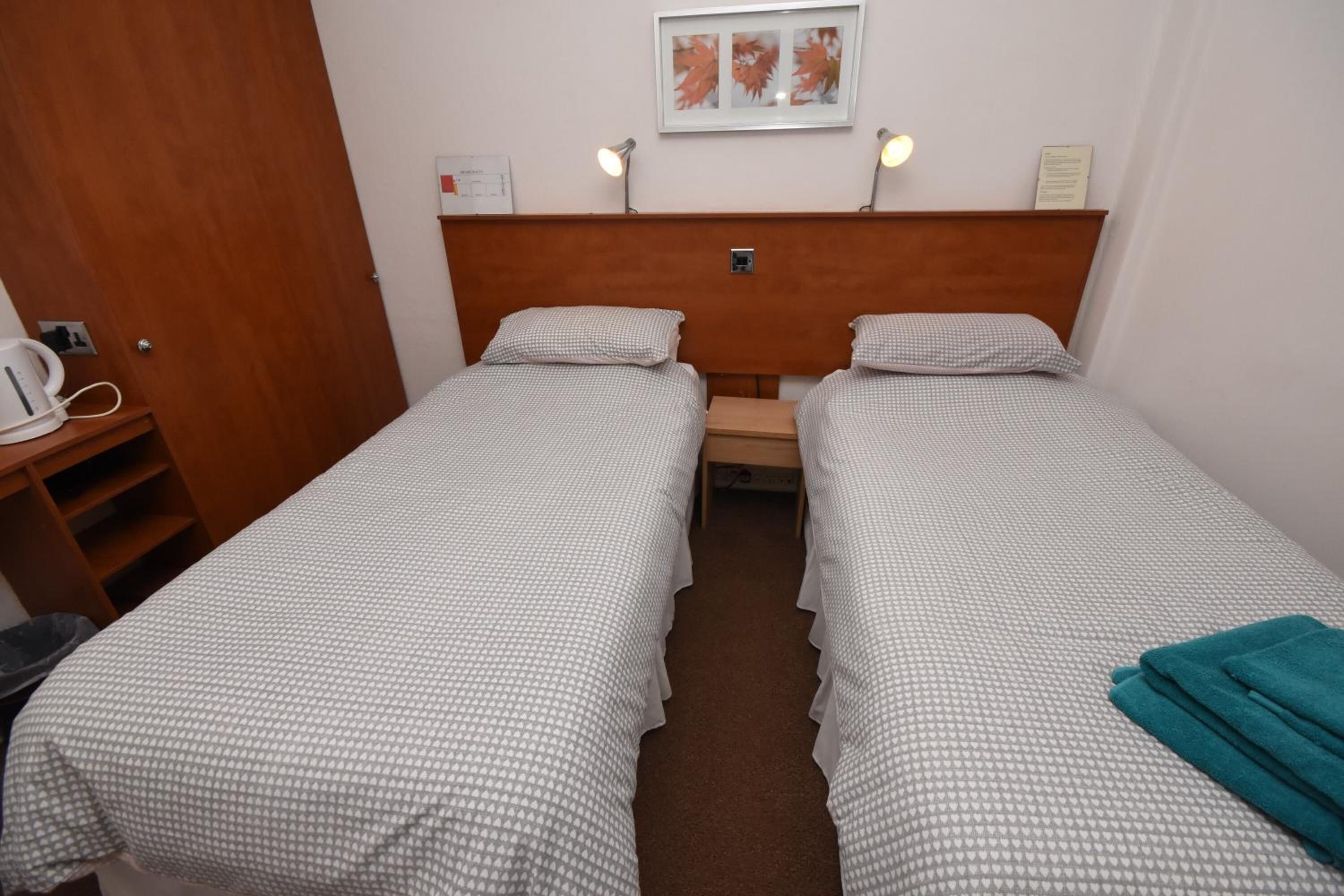 A twin room with two single beds, a wooden headboard, a small table, and a wall-mounted lamp.