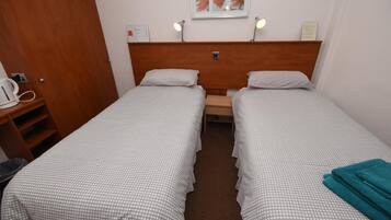 A twin room with two single beds, a wooden headboard, a small table, and a wall-mounted lamp.