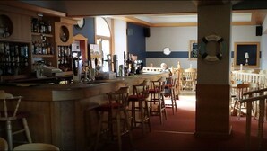 Una zona de bar con sillas y mesas de madera, una barra con diferentes botellas y un reloj en la pared.