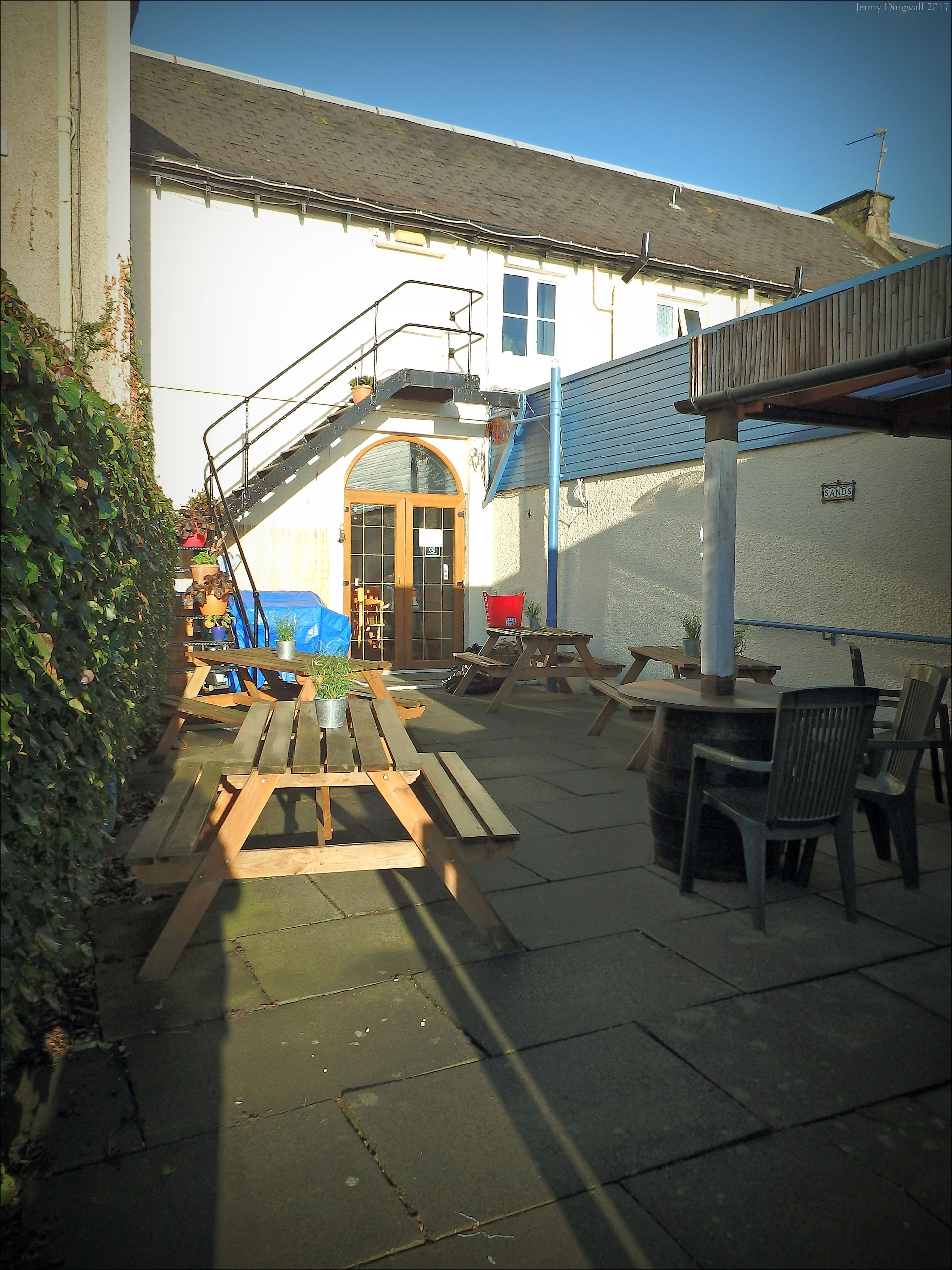 Ein Innenhof mit Holzbänken und -tischen, einer Treppe und einem Gebäude mit blauem Dach.