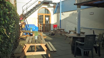 Ein Innenhof mit Holzbänken und -tischen, einer Treppe und einem Gebäude mit blauem Dach.
