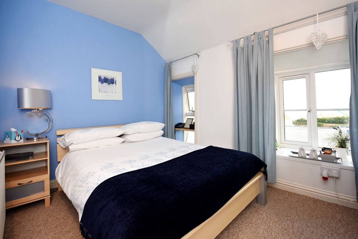 A bedroom with a bed, bedside table, lamp, and a window with curtains.