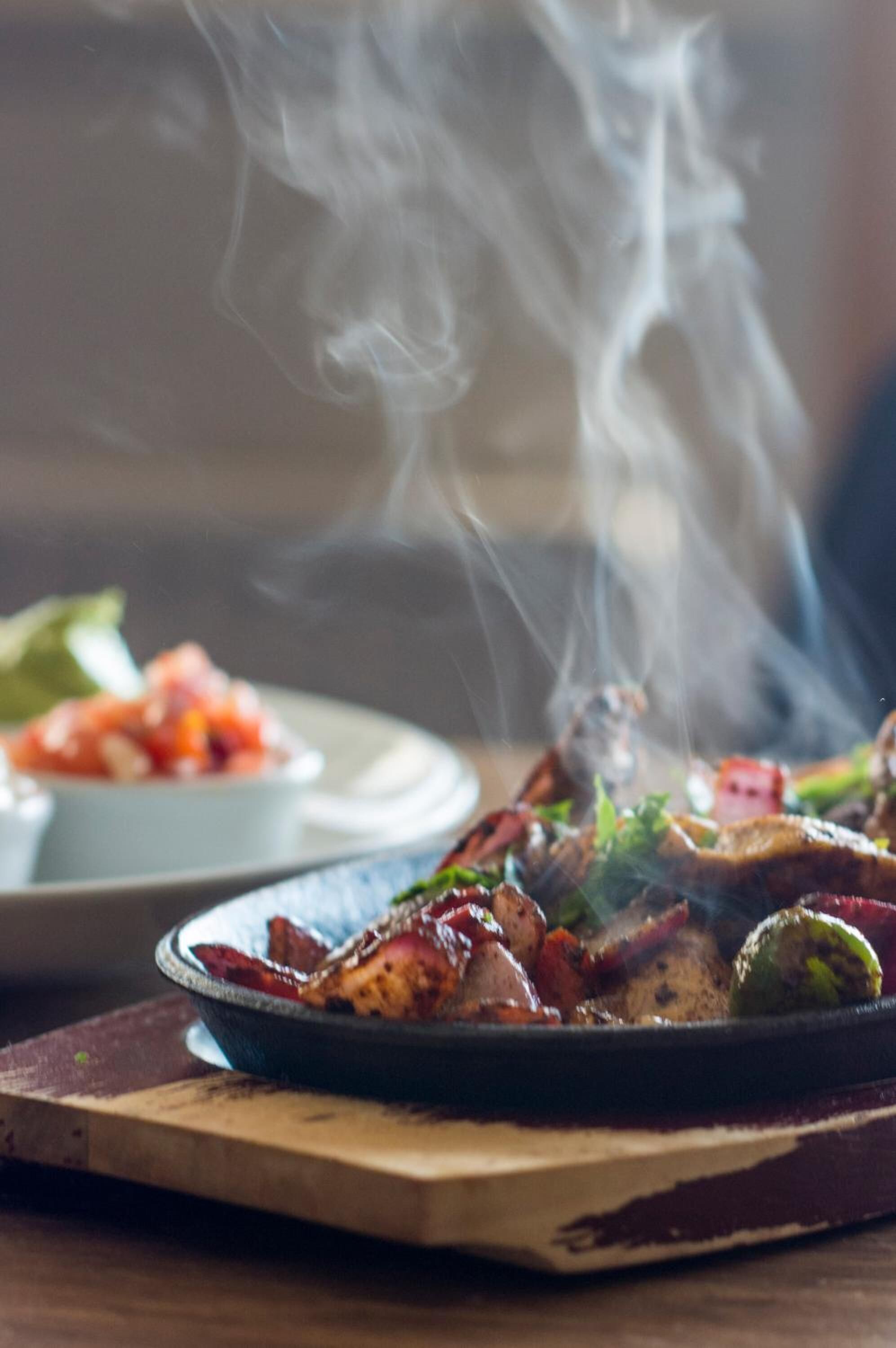 A plate of food with smoke rising from it, placed on a wooden board.