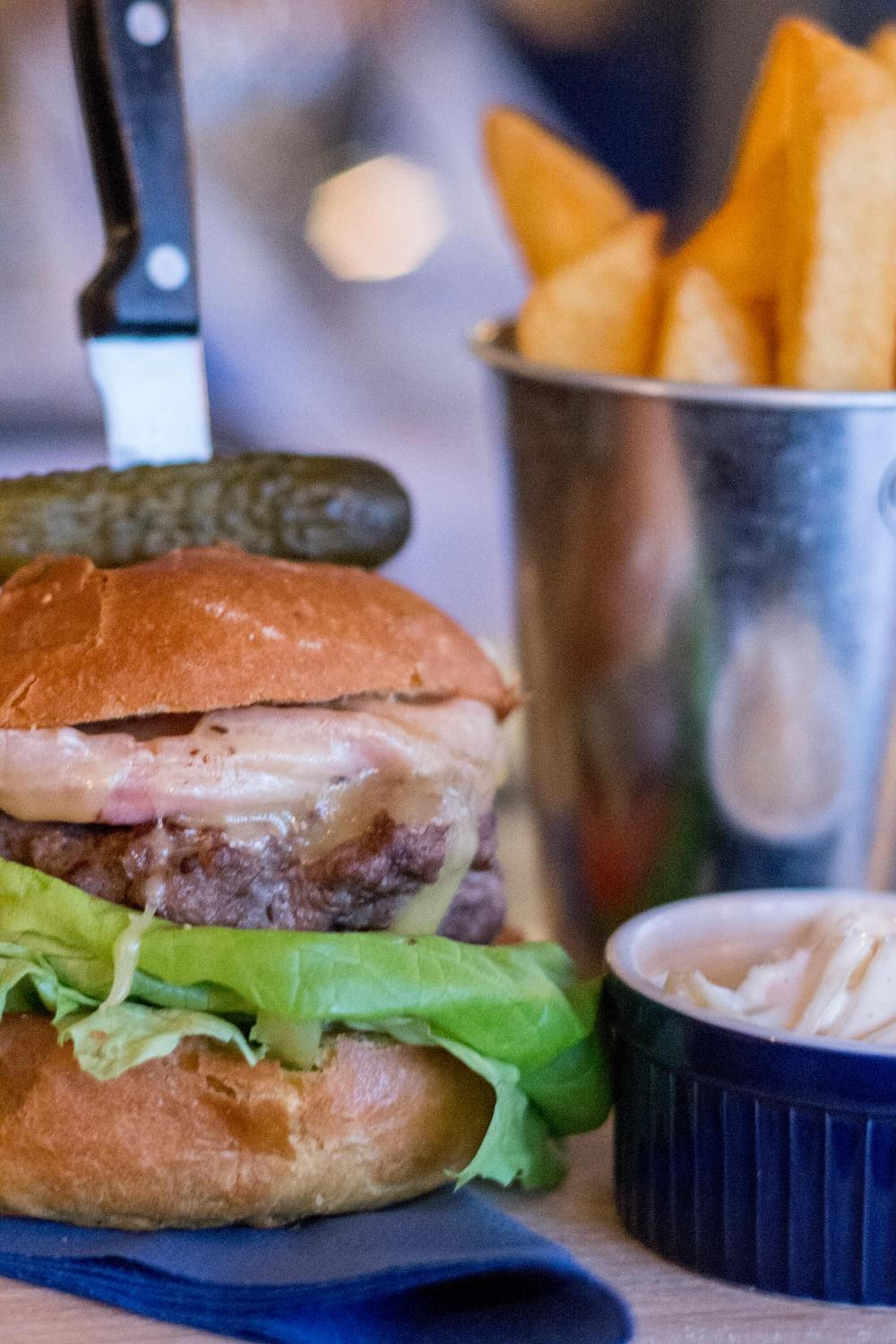 Ein Burger mit Pommes und Gurke auf einem Holztisch.