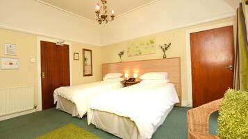 Habitación de hotel con dos camas individuales, cabecero de madera, alfombra verde, candelabro y una puerta con cortina.