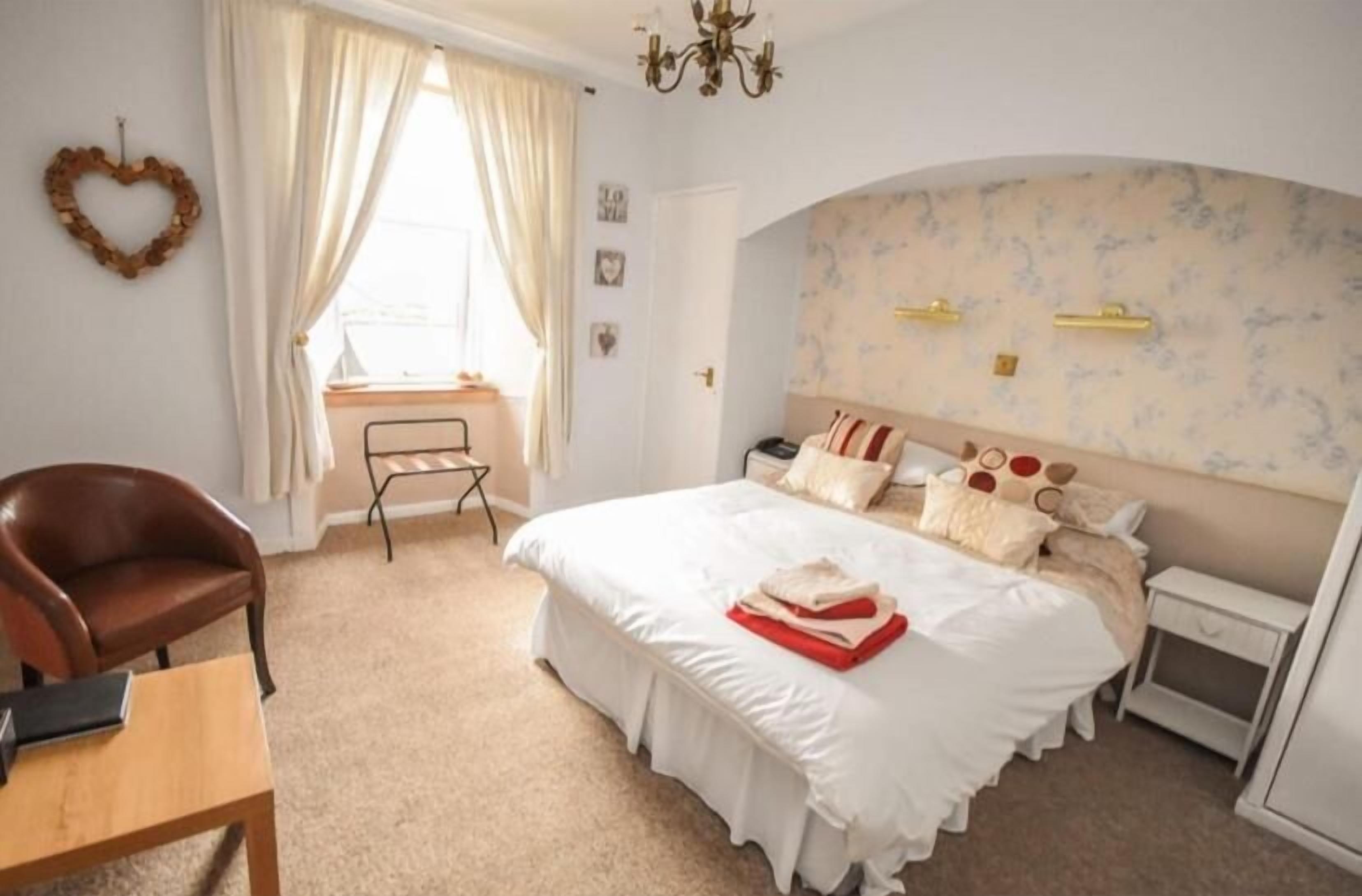 Een slaapkamer met een groot bed, een stoel, een bureau en een klein tafeltje.