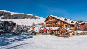 A wooden lodge with a balcony, surrounded by snow-covered trees and a clear blue sky.