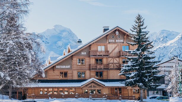 A wooden chalet with a bar and restaurant on the upper level, surrounded by snow-covered mountains.