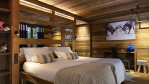 Een slaapkamer in hout met een groot bed, een bureau met een laptop en een schilderij van rendieren.
