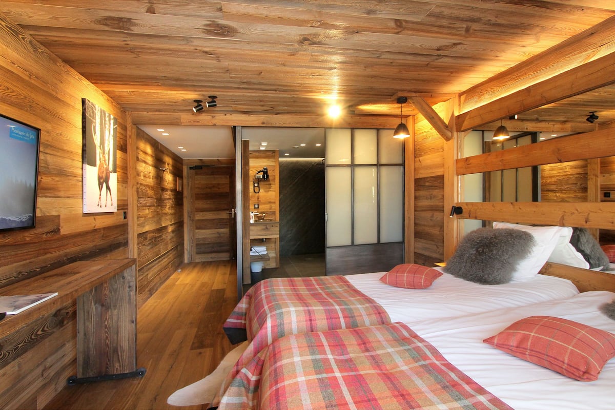 Un dormitorio tipo cabaña de madera con cama, almohadas y un televisor sobre una pared de madera.