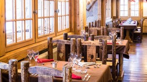 Een rustiek houten interieur met hoge plafonds en grote ramen. Tafels zijn gedekt voor het diner, met stoelen.