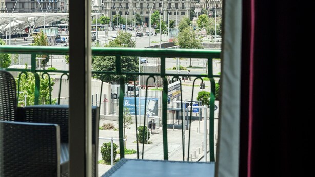 A balcony with wicker chairs and a table, overlooking a cityscape with buildings and a dome structure. - B&B Metropolitan (Naples)