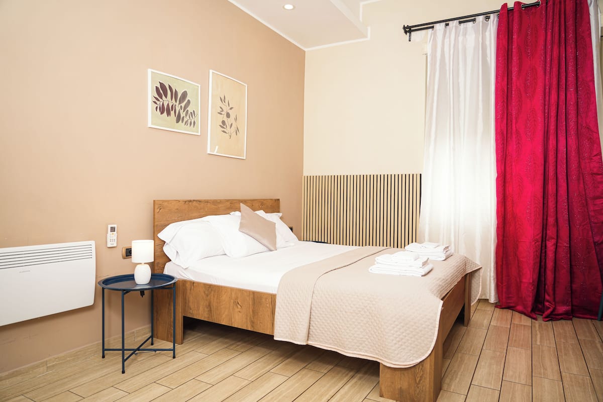 A neatly arranged hotel room with a wooden bed, a bedside table with a lamp, and two wall-mounted artworks.