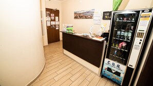 A reception area with a wooden reception desk, a Coda vending machine, and a green flag on the wall. - B&B Metropolitan (Naples)