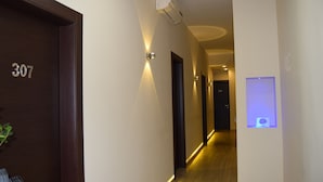 A hotel hallway with a wooden door labeled "307", a wall-mounted air conditioner, and a wall-mounted light fixture. - B&B Metropolitan (Naples)