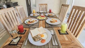Une table de petit-déjeuner avec une table en bois, des chaises et une variété d'aliments, notamment des œufs, des toasts et des boissons.