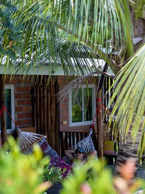 A small brick building with two hammocks tied to the roof, surrounded by lush greenery. - Cat Bungalow (Ko Lanta)