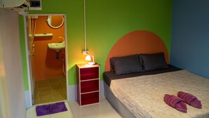 Un dormitorio con cama, una mesita de noche con lámpara, un espejo y un baño a la vista a través de una puerta abierta.