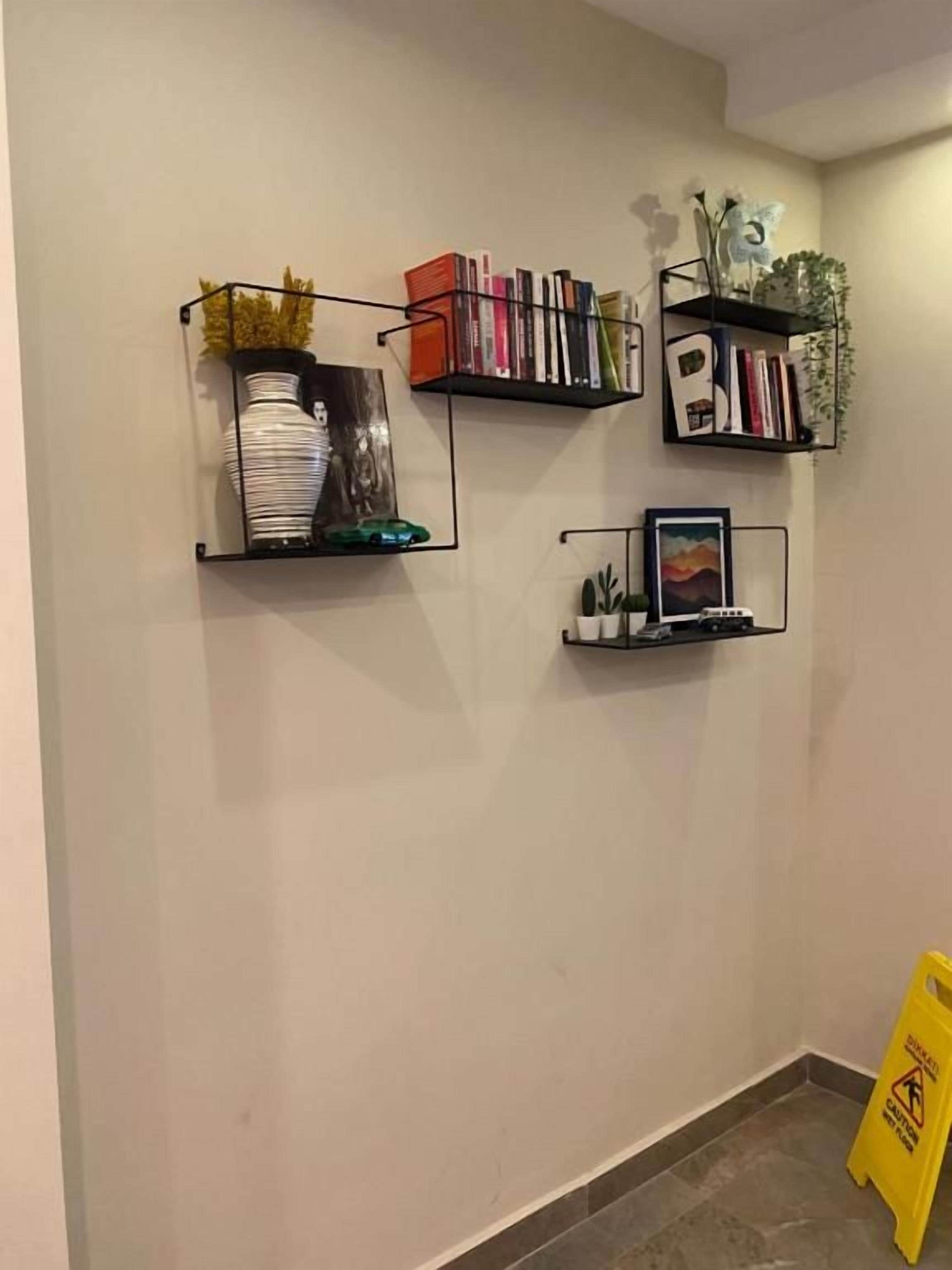 A wall with three black metal shelves, each holding various items like books, decorative objects, and small plants.