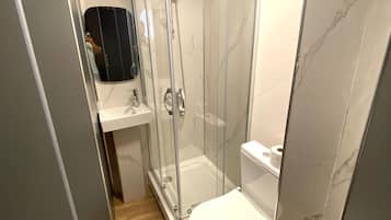 Casa de banho compacta com chuveiro envolto em vidro, sanita e lavatório.