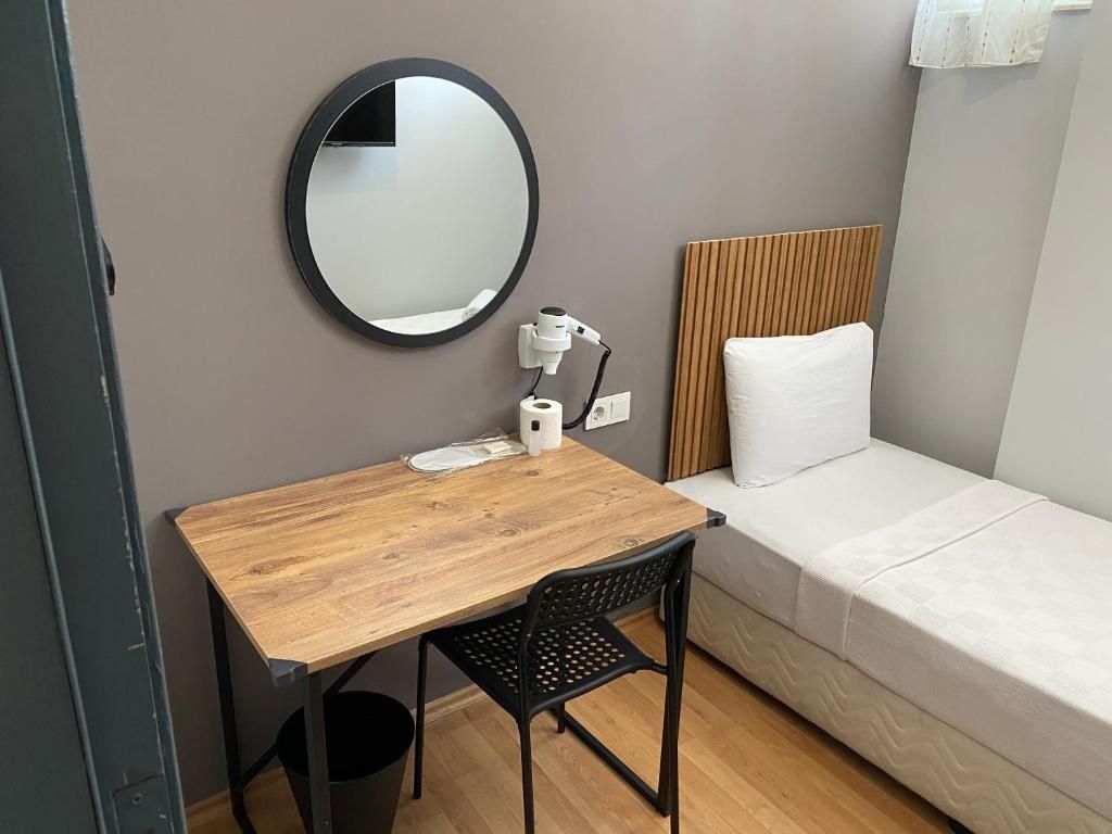 Une pièce de taille modeste, avec un bureau en bois, un miroir rond, un coussin blanc et une petite poubelle.