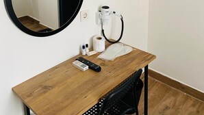 Um quarto pequeno com uma escrivaninha de madeira, um espelho redondo, um secador de cabelo e um porta-toalhas.