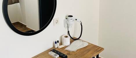 A small room with a wooden desk, a round mirror, a hairdryer, and a towel rack.