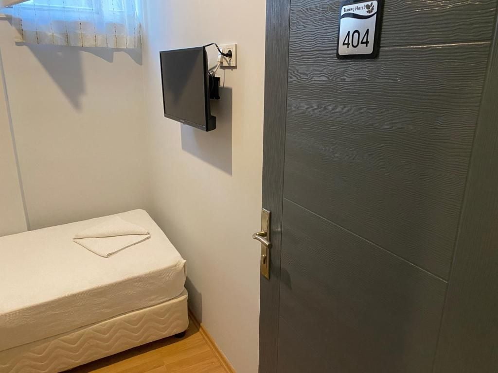 Una camera d'albergo con un letto, una TV a parete e una porta con il numero della stanza.