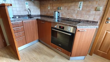 A compact kitchen with wooden cabinets, a Bosch oven, a stainless steel sink, and a granite countertop.