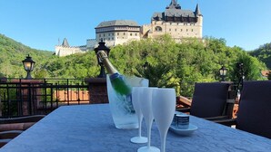 Una mesa con una botella de champán, dos copas y un bol pequeño en una terraza con vistas a un castillo.