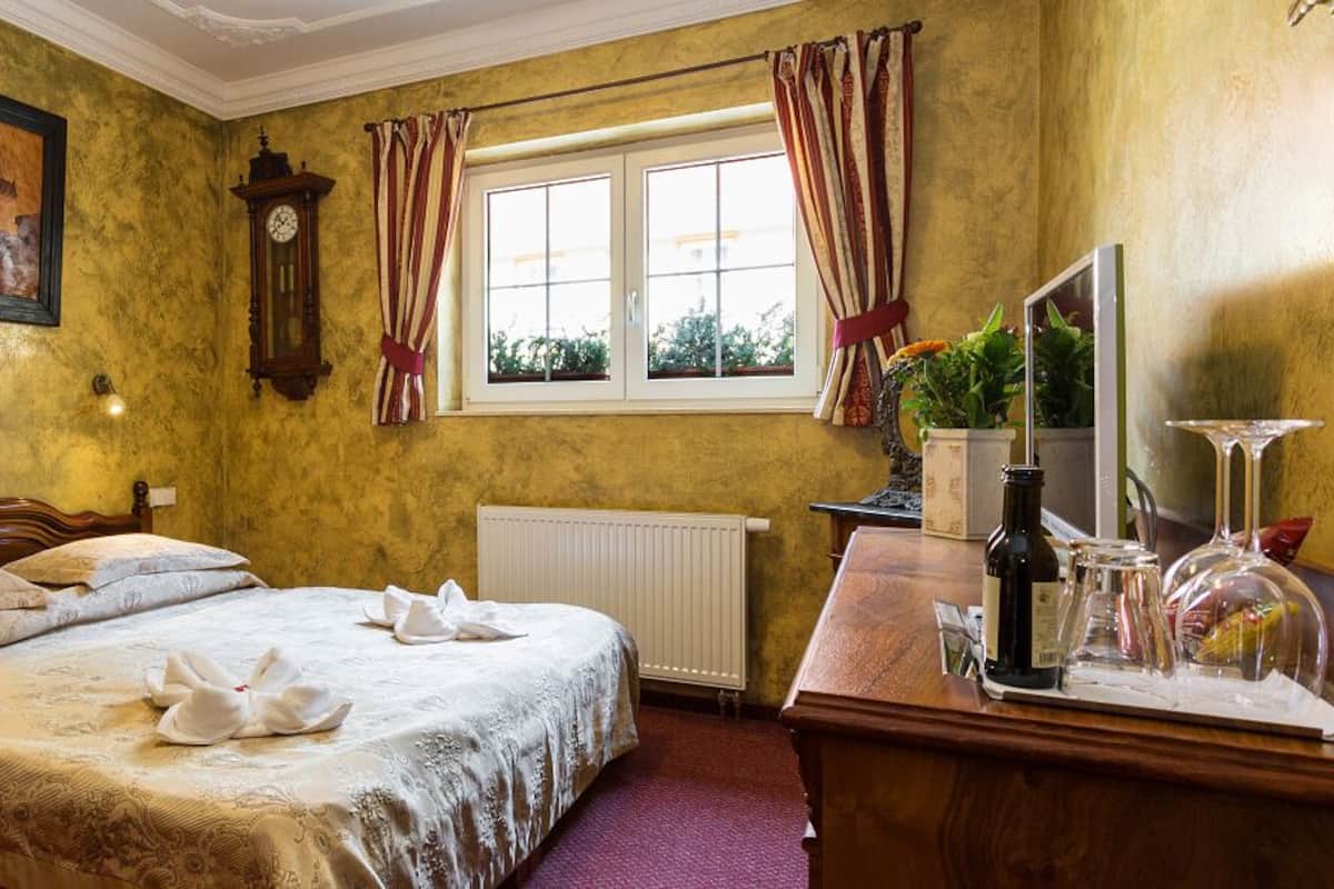 A hotel room with a bed, a wooden nightstand, a desk with a mirror, a clock, and a window with curtains.