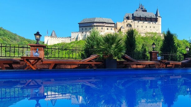 Una piscina con sillones de descanso y vista a un edificio parecido a un castillo al fondo.