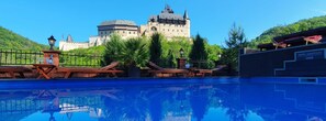 A swimming pool with lounge chairs and a view of a castle-like building in the background. - Hotel Karlštejn (Karlstejn)