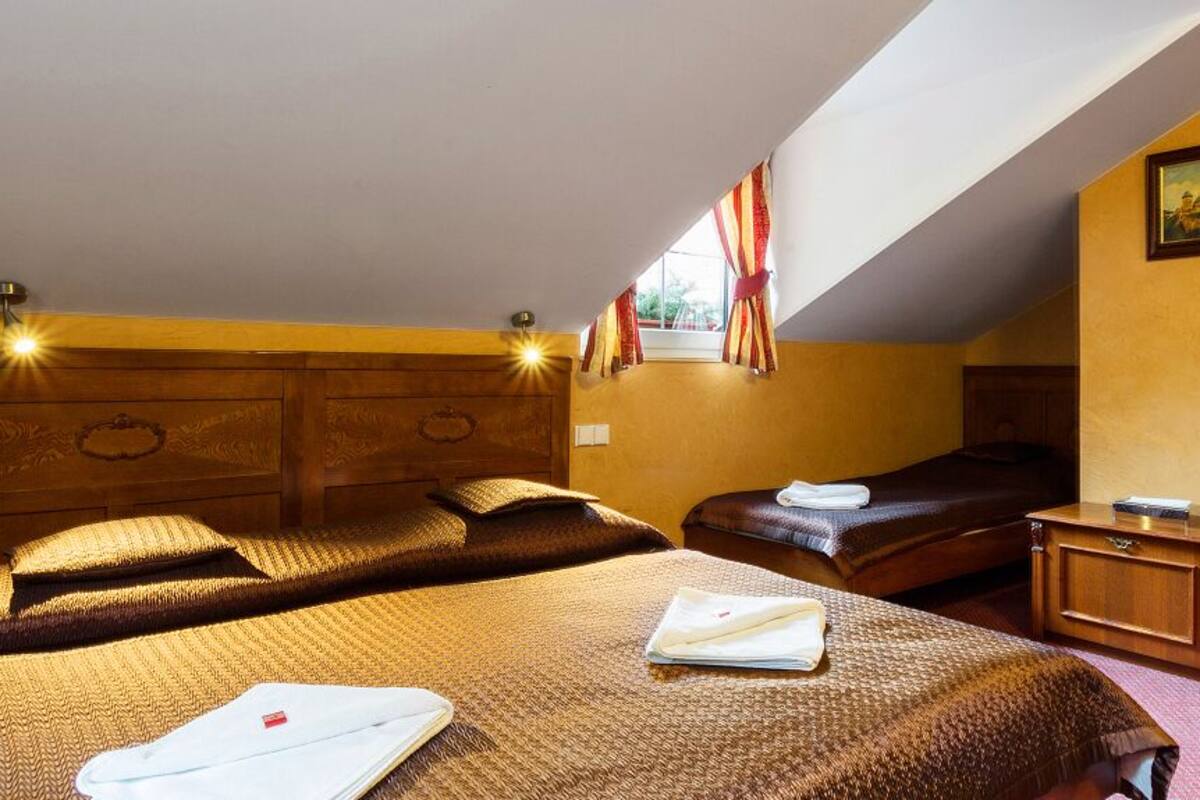 A hotel room with two beds, a wooden headboard, a small table, and a window with curtains.