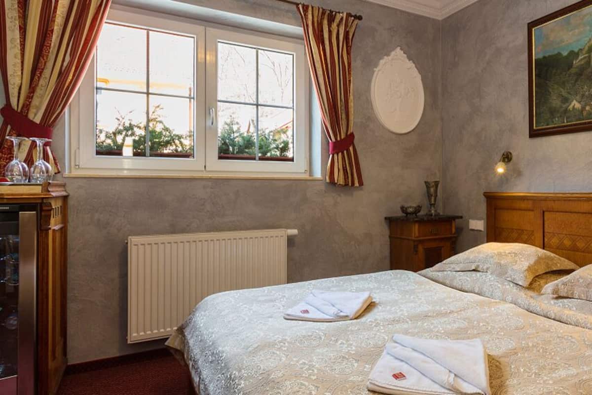 A hotel room with a double bed, a radiator, a window with curtains, a painting on the wall, and a bedside table with a lamp.