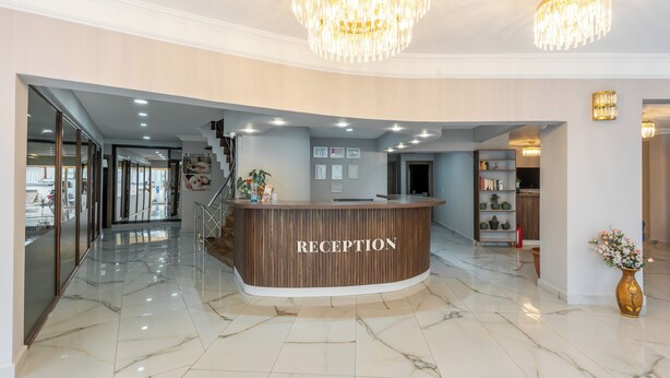 A reception area with a marble floor, a wooden reception desk, and a chandelier. - Safari Otel (Antalya)