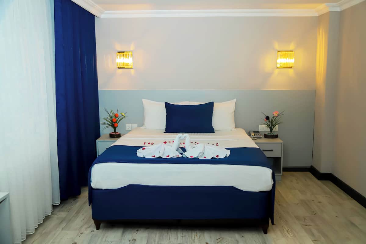 A hotel room with a bed, two bedside tables, a nightstand, a lamp, and a wall-mounted light fixture.