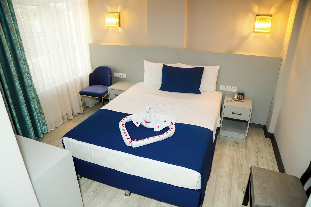 A hotel room with a large bed, a bedside table, a chair, and a desk.