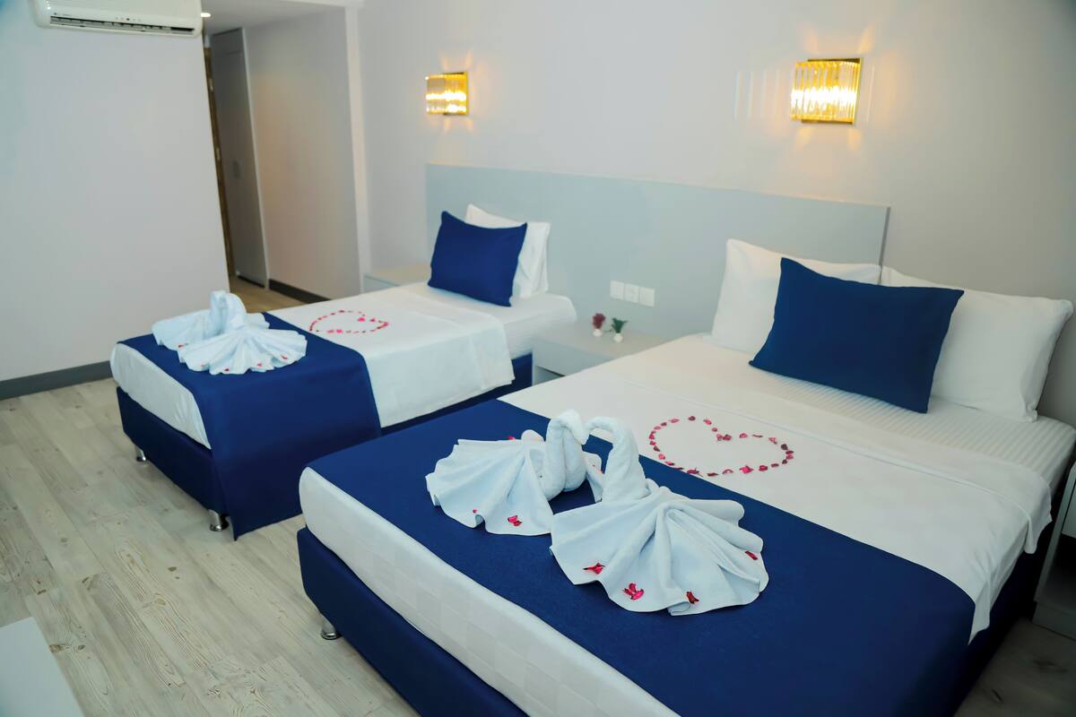 Two hotel beds with blue bedding and white pillows, each adorned with a heart-shaped towel arrangement.