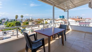 A balcony with a table and chairs, offering a view of a cityscape with buildings and palm trees. - Safari Otel (Antalya)